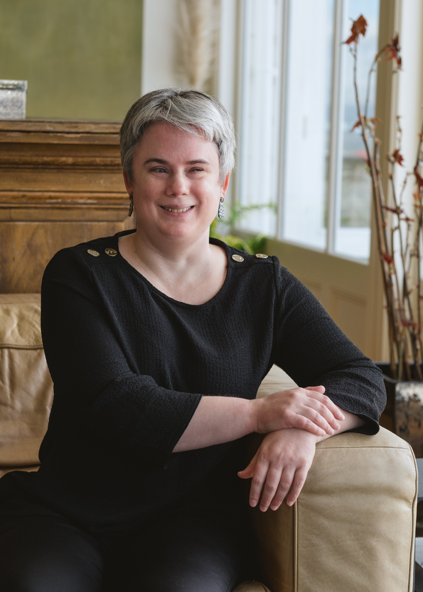 Lauren Hayes smiling, seated on a sofa near a window